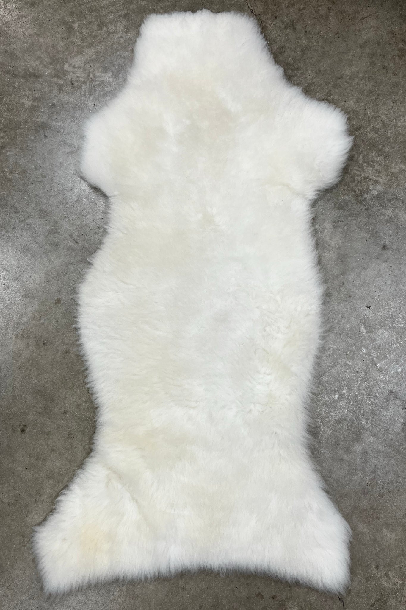 A fluffy white sheepskin rug laid flat on a gray concrete floor.