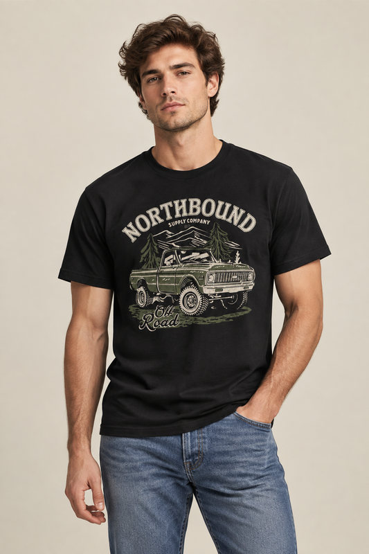 A man wearing a black graphic t-shirt with a vintage green truck and 'NORTHBOUND SUPPLY COMPANY' print, paired with blue jeans, against a neutral beige background.