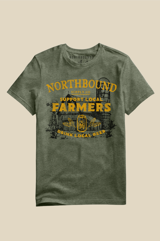An olive green heathered t-shirt with a vintage-style graphic on the front. The graphic features a farm illustration with a silo and a beer mug, accompanied by yellow text reading 'NORTHBOUND', 'SUPPORT LOCAL FARMERS', and 'DRINK LOCAL BEER'.