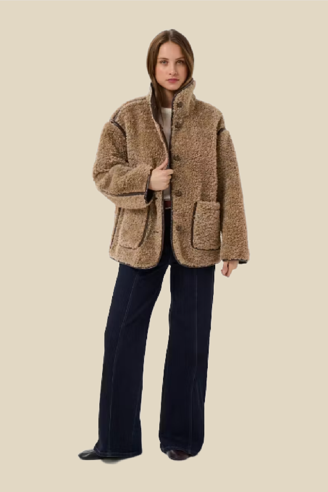 A woman modeling a brown sherpa fleece jacket with dark navy wide-leg jeans against a solid beige background.