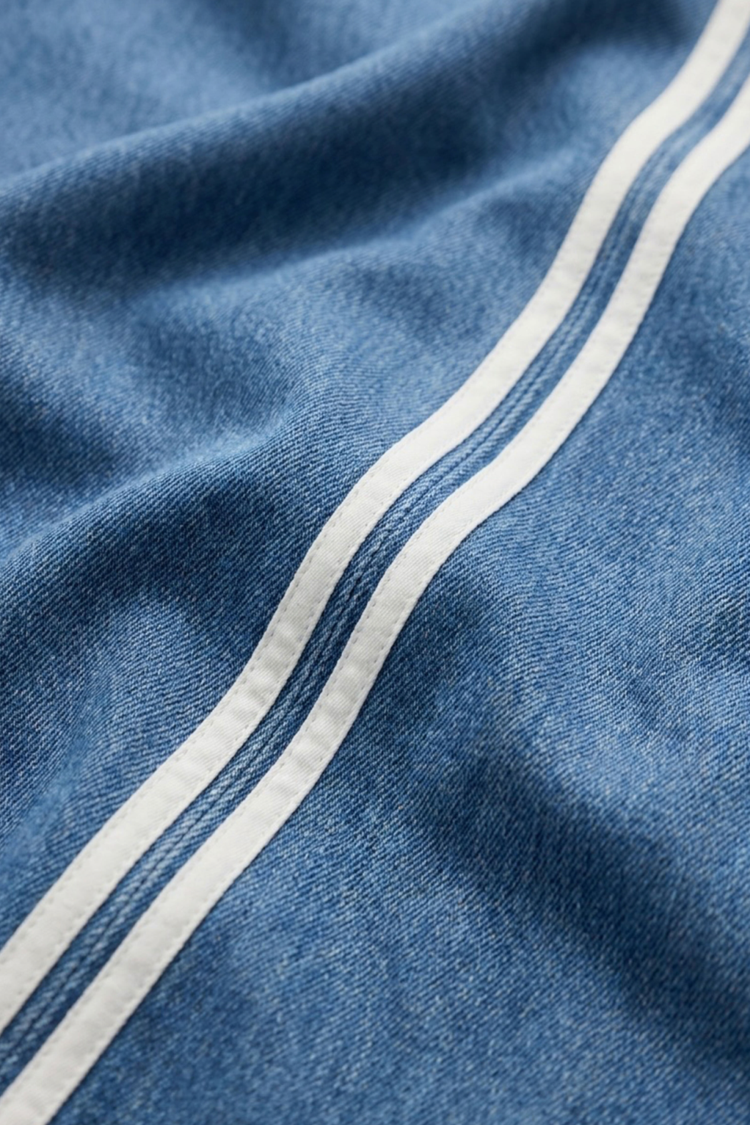 Close-up of blue denim fabric with two parallel white stripes running diagonally across the frame.